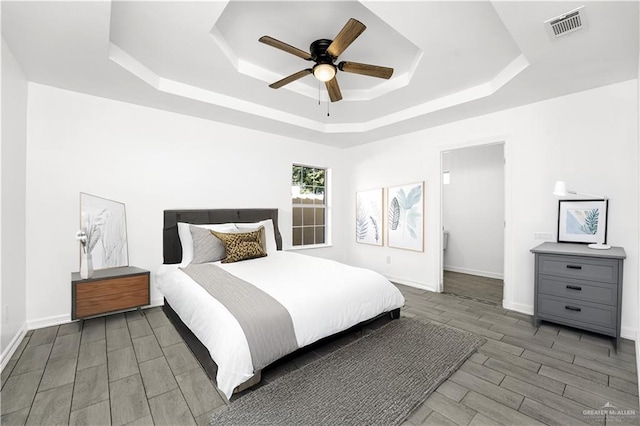 bedroom with dark hardwood / wood-style flooring, a raised ceiling, and ceiling fan