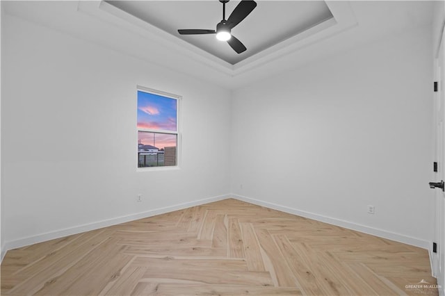 unfurnished room featuring a raised ceiling, ceiling fan, and light parquet flooring