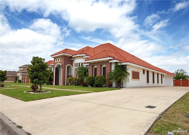 mediterranean / spanish-style house with a garage, a tile roof, concrete driveway, stucco siding, and a front lawn