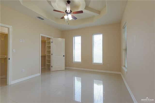 unfurnished bedroom featuring a walk in closet, light tile patterned floors, a raised ceiling, visible vents, and baseboards