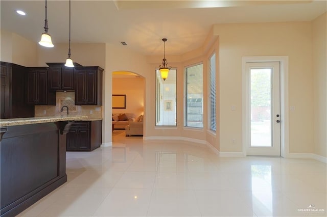 kitchen featuring hanging light fixtures, dark brown cabinetry, arched walkways, and backsplash