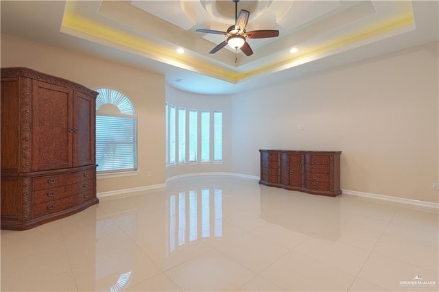 empty room featuring a ceiling fan, a raised ceiling, baseboards, and light tile patterned floors