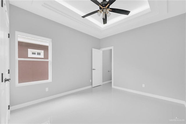 spare room with a tray ceiling, a ceiling fan, and baseboards