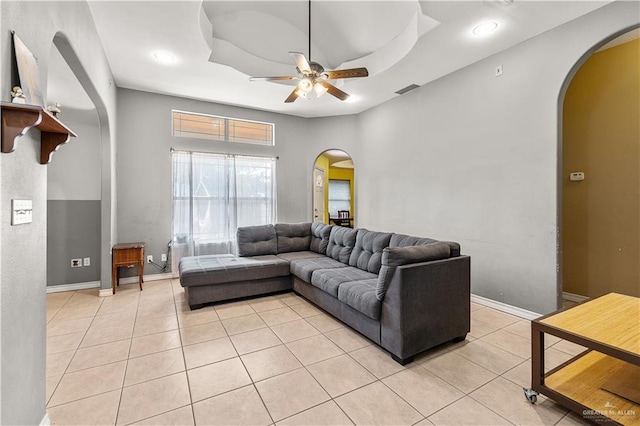 tiled living room with ceiling fan and a tray ceiling