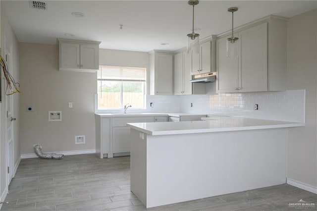 kitchen featuring sink, hanging light fixtures, kitchen peninsula, decorative backsplash, and light wood-type flooring