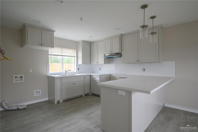 kitchen with kitchen peninsula, a kitchen breakfast bar, sink, light hardwood / wood-style flooring, and hanging light fixtures