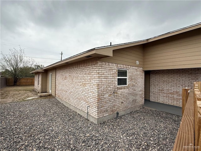 view of side of home featuring a patio area, fence, and brick siding