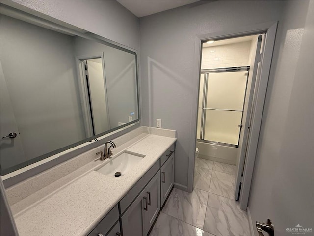 bathroom featuring marble finish floor, toilet, enclosed tub / shower combo, vanity, and baseboards