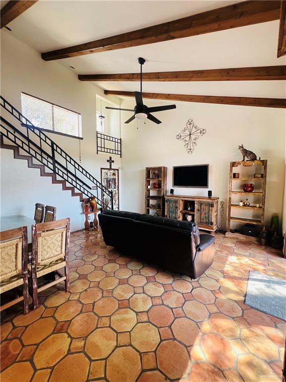 living room with a ceiling fan, beam ceiling, and stairway