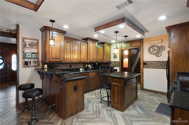 2820 Joan Dr, Edinburg, TX 78541 - kitchen featuring dark countertops, a peninsula, a breakfast bar area, brown cabinetry, and decorative backsplash