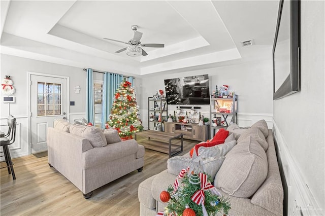 living room with ceiling fan, a raised ceiling, and light hardwood / wood-style flooring