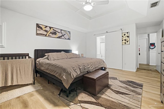 bedroom with ceiling fan, a barn door, a raised ceiling, and light hardwood / wood-style flooring