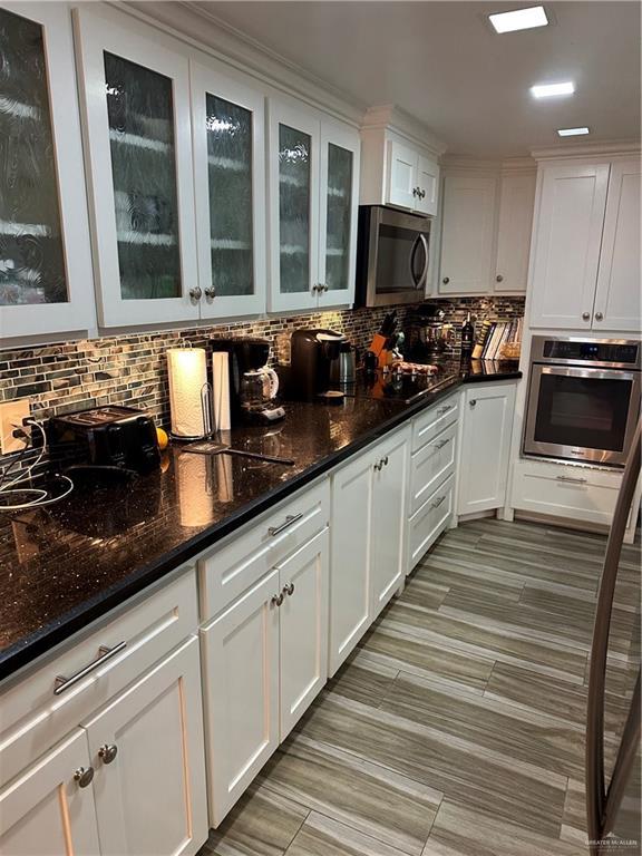 42 E Cherokee Dr, Harlingen, TX 78550 - kitchen with stainless steel appliances, white cabinetry, backsplash, dark stone countertops, and glass insert cabinets