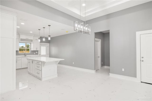 kitchen featuring white cabinets, a center island, decorative light fixtures, and sink