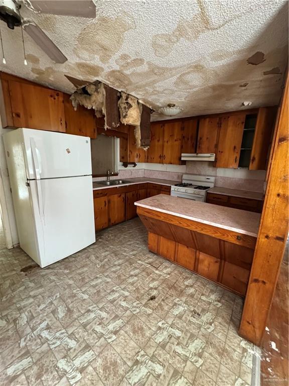 kitchen featuring kitchen peninsula, a textured ceiling, white appliances, ceiling fan, and sink