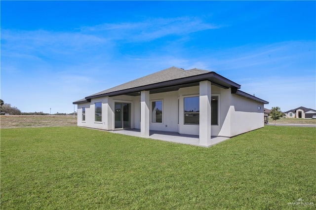 back of property with roof with shingles, a patio area, a lawn, and stucco siding