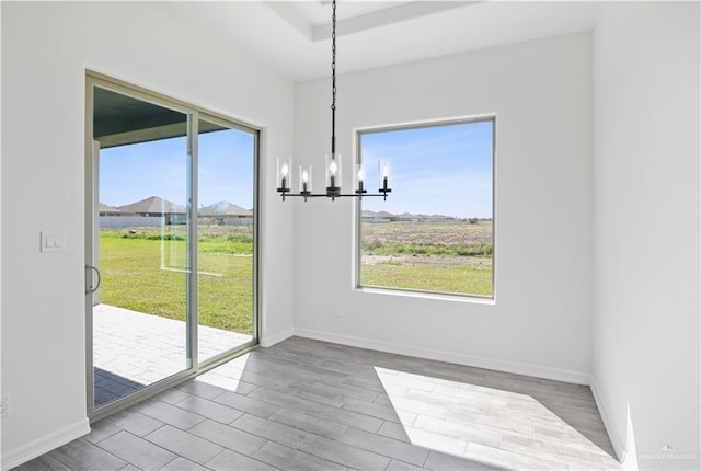 unfurnished dining area with a chandelier, a raised ceiling, baseboards, and wood finished floors