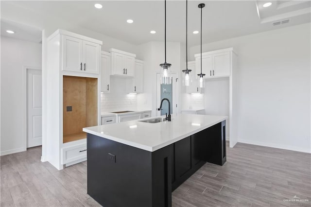 kitchen featuring tasteful backsplash, light wood-style flooring, white cabinets, a sink, and an island with sink