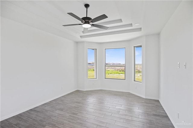 spare room with wood finished floors, a raised ceiling, a ceiling fan, and baseboards