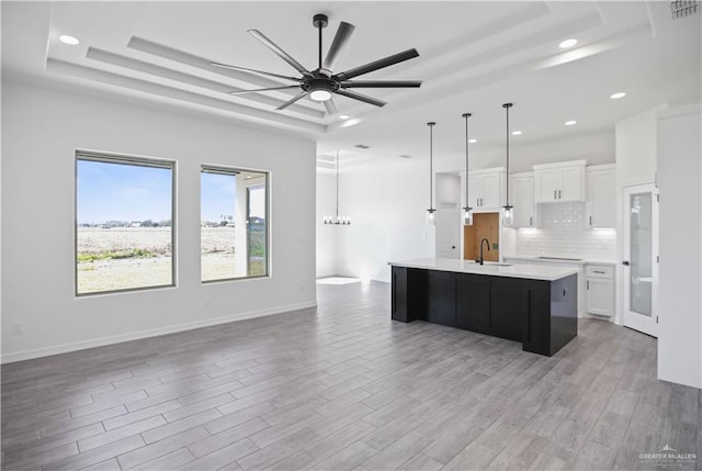 kitchen with white cabinets, light wood-style flooring, a raised ceiling, and a sink