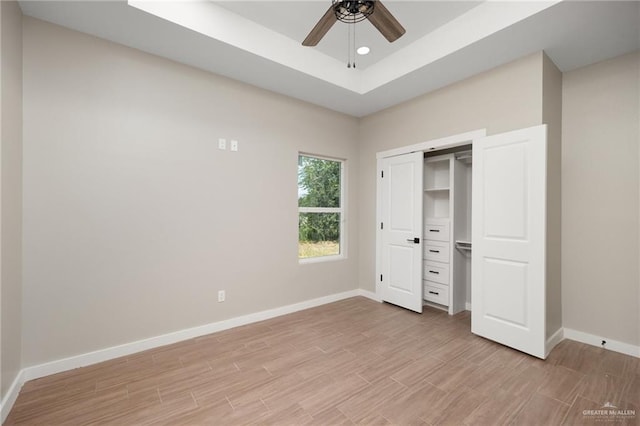 unfurnished bedroom with a tray ceiling, ceiling fan, a closet, and light wood-type flooring