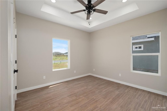 spare room featuring a tray ceiling, light hardwood / wood-style flooring, and ceiling fan