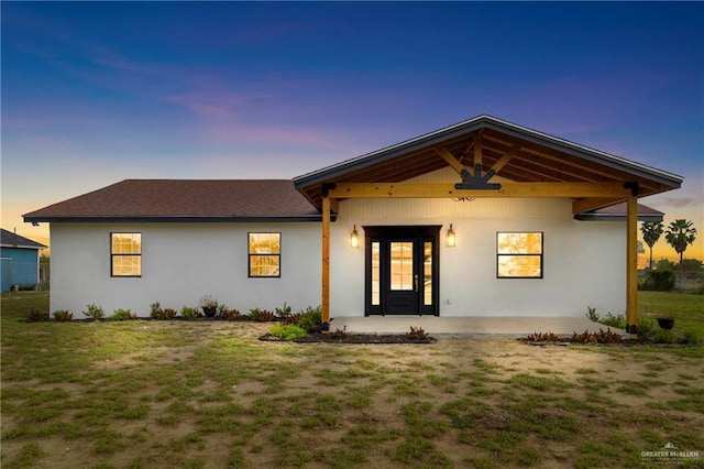 view of front facade with a patio area, roof with shingles, a lawn, and stucco siding