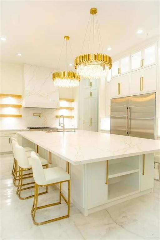 kitchen with a large island with sink, white cabinetry, built in refrigerator, and hanging light fixtures