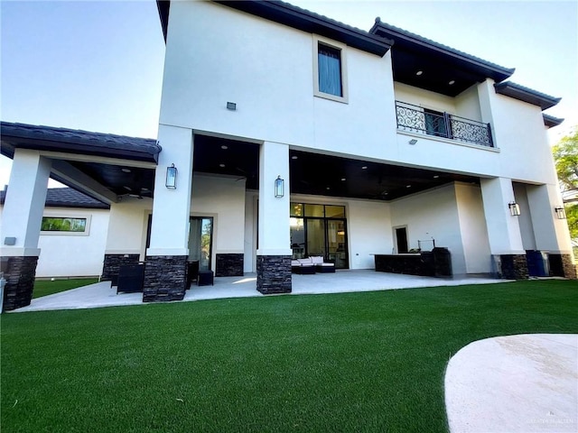 back of house featuring ceiling fan, a balcony, a yard, and a patio