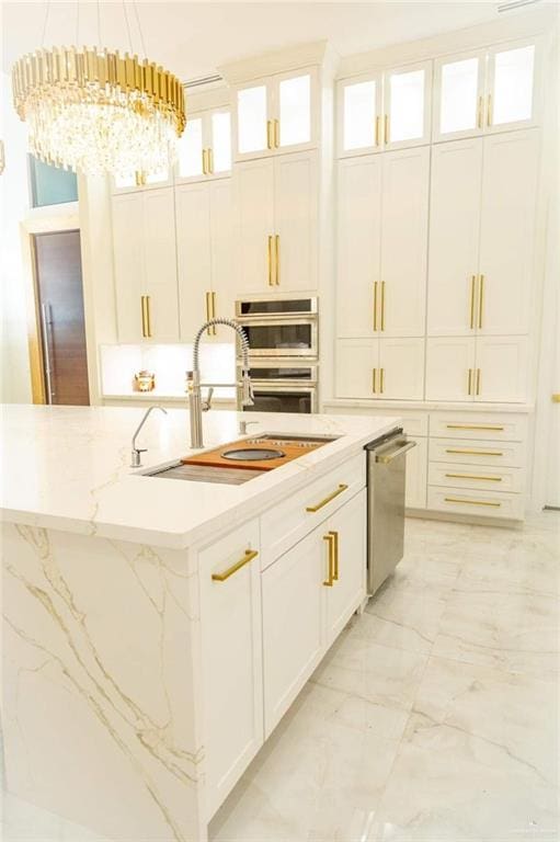 kitchen featuring an inviting chandelier, sink, an island with sink, decorative light fixtures, and white cabinetry