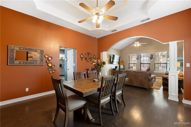 dining area with ceiling fan, a raised ceiling, ornate columns, and dark wood-type flooring