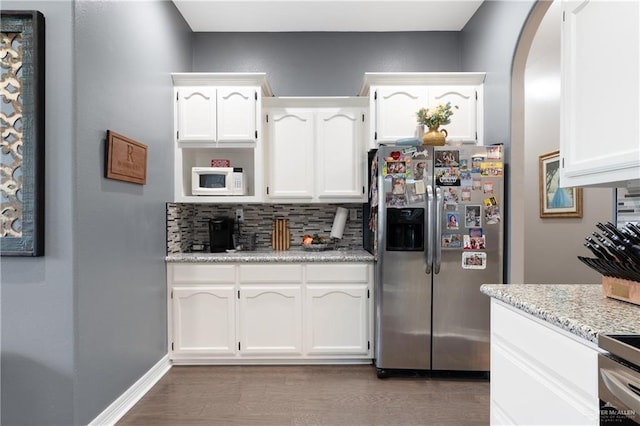 kitchen featuring backsplash, dark wood-type flooring, white cabinets, appliances with stainless steel finishes, and light stone counters