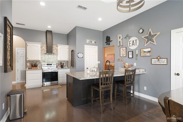 kitchen with light stone counters, wall chimney exhaust hood, white cabinets, a breakfast bar area, and stainless steel electric range