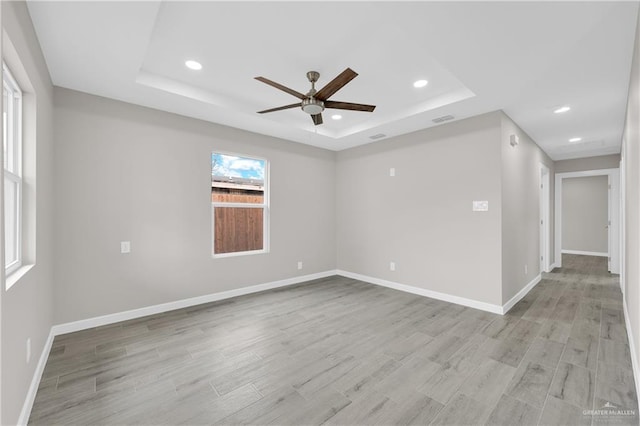 empty room featuring recessed lighting, a raised ceiling, visible vents, light wood-type flooring, and baseboards