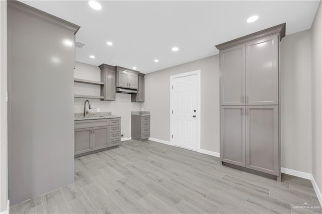 kitchen featuring gray cabinets, a sink, light wood-style flooring, and open shelves