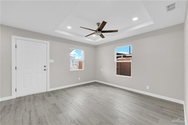 empty room featuring light wood-type flooring, a tray ceiling, visible vents, and baseboards