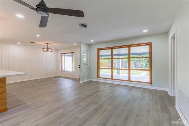 unfurnished living room featuring ceiling fan with notable chandelier and light hardwood / wood-style flooring