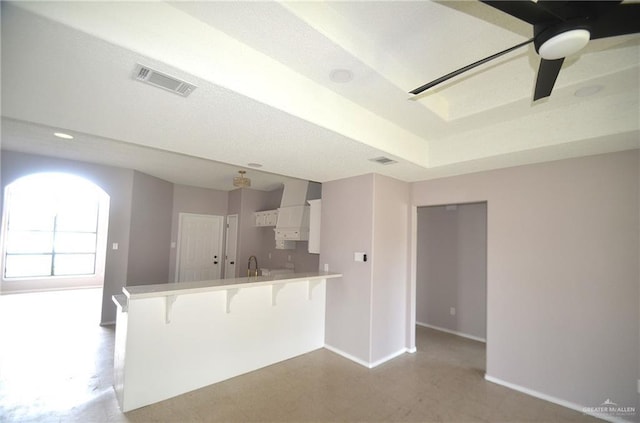 3107 E Laurel St, Hidalgo, TX 78557 - kitchen with a peninsula, white cabinets, a breakfast bar area, baseboards, and wall chimney range hood