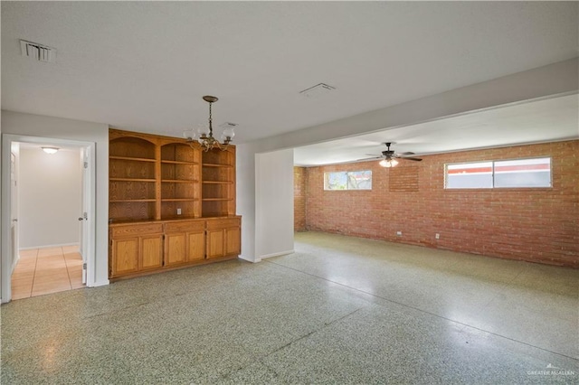 206 E Ricky Crossland Ave, Elsa, TX 78543 - unfurnished living room with brick wall, dark speckled floor, plenty of natural light, a chandelier, and a ceiling fan