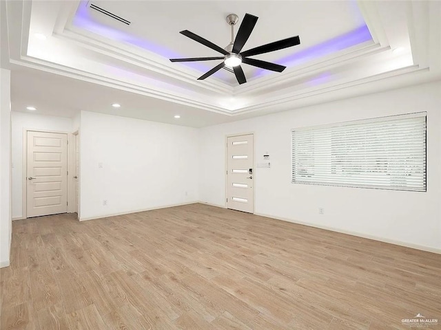 empty room with light wood finished floors, a raised ceiling, a ceiling fan, recessed lighting, and visible vents