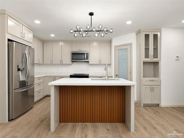 kitchen with appliances with stainless steel finishes, light wood-type flooring, a sink, an inviting chandelier, and an island with sink