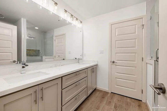 bathroom with a sink, double vanity, baseboards, wood finished floors, and a shower with door