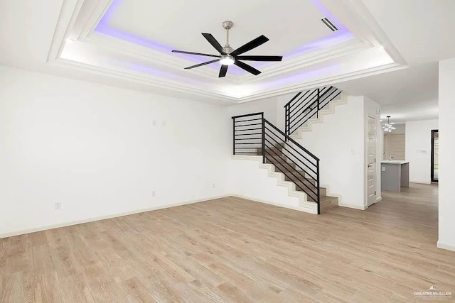 unfurnished living room with stairway, light wood-type flooring, a tray ceiling, a sink, and ceiling fan with notable chandelier
