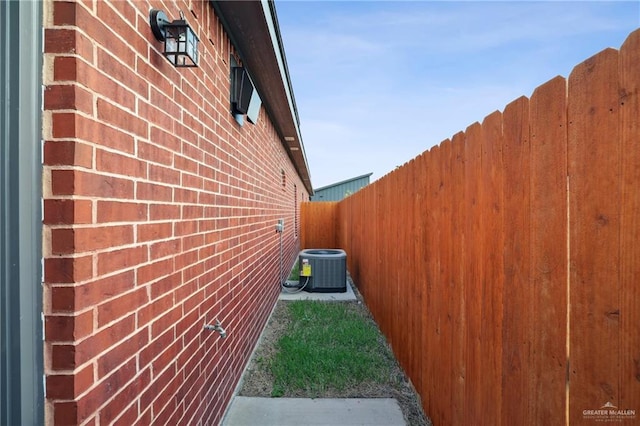 view of side of home featuring brick siding, central AC unit, and fence