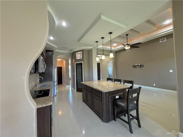 kitchen featuring decorative backsplash, light stone countertops, a breakfast bar, ceiling fan, and a kitchen island