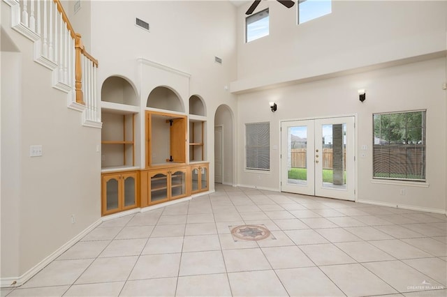 empty room featuring built in shelves, a wealth of natural light, light tile patterned flooring, and a high ceiling