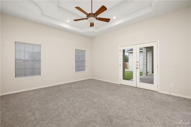 carpeted empty room with ceiling fan, a raised ceiling, and french doors