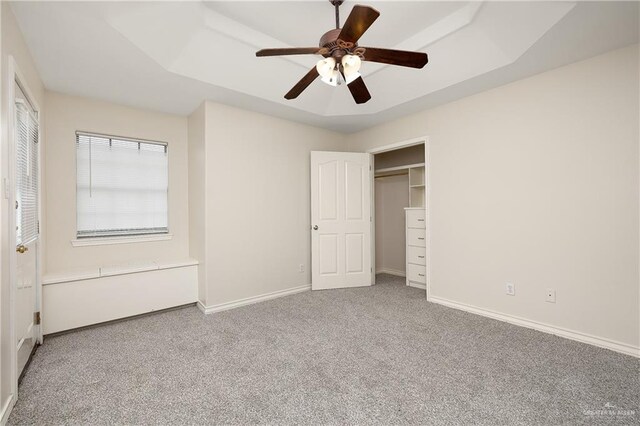 unfurnished bedroom with ceiling fan, a raised ceiling, and carpet floors