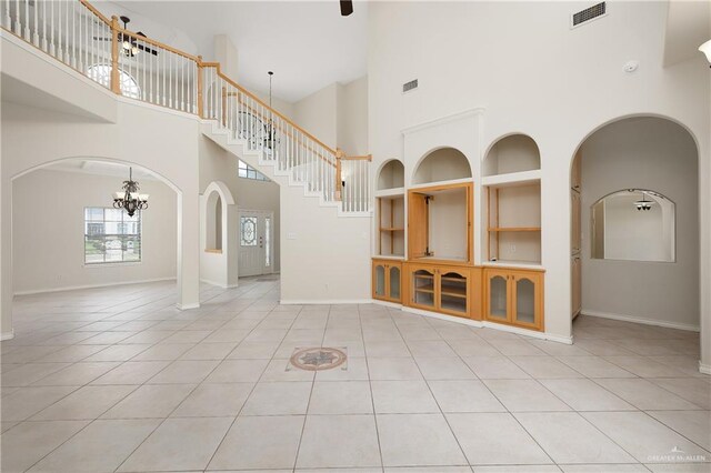 unfurnished living room featuring built in shelves, light tile patterned flooring, and a towering ceiling