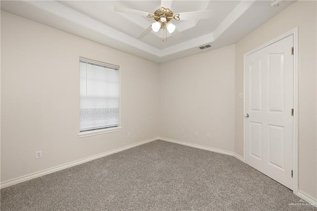 carpeted spare room with a tray ceiling and ceiling fan